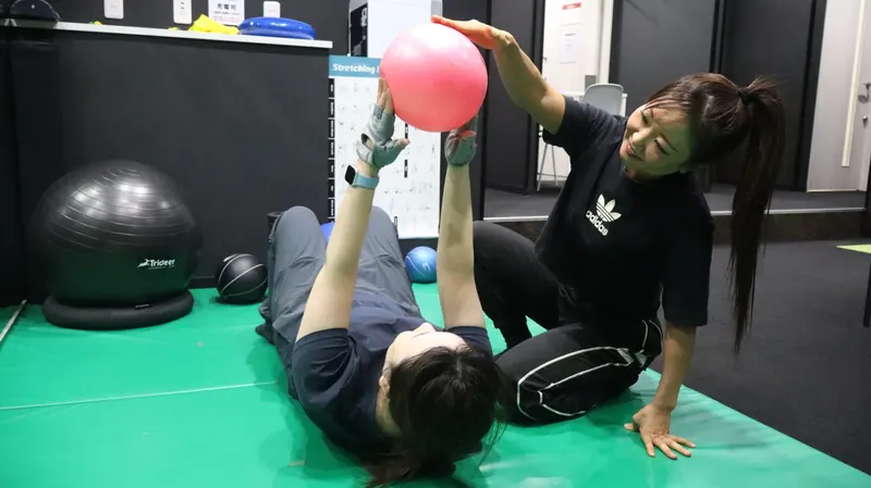 トレーナーと一緒にボールを使って体を動かす